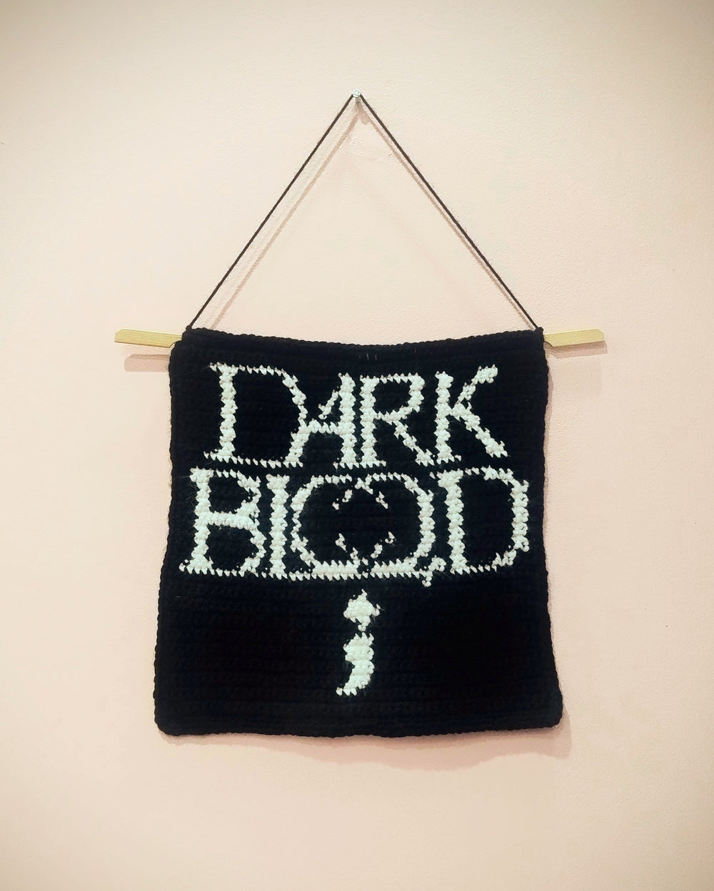 Large handmade black crochet wall banner with cream lettering, hung on a wooden dowel