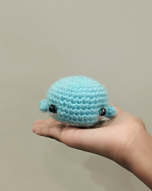 Small handmade crochet whale in ocean blue held in an open palm