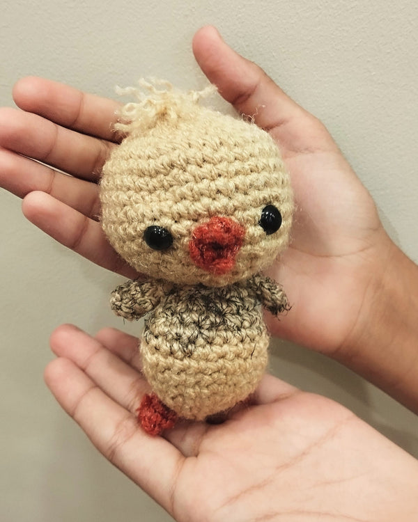 Small handmade crochet chick with a cream body and orange beak held in two hands