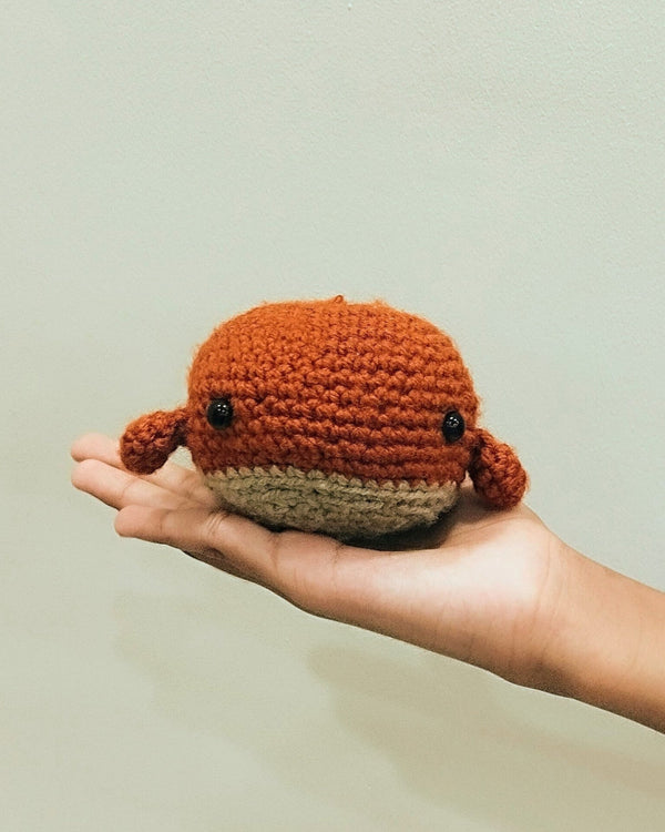 Small handmade crochet chick with a cream body and orange beak held in two hands