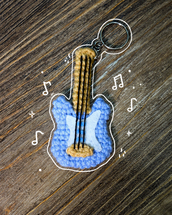 Handmade blue crochet guitar keychain with a silver key ring on a wooden surface