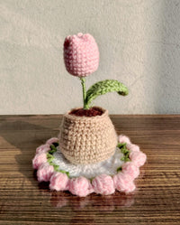 Handmade crochet pink tulip in a rustic brown pot resting on a book